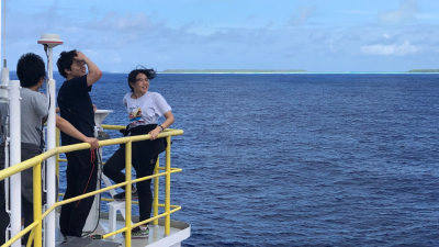 Kazatuka, Hojun und Wendy an Deck, Korallenatoll im Hintergrund.