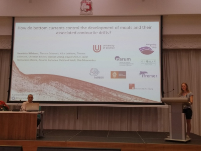 Henriette in front of a big screen that shows the first slide of her presentation