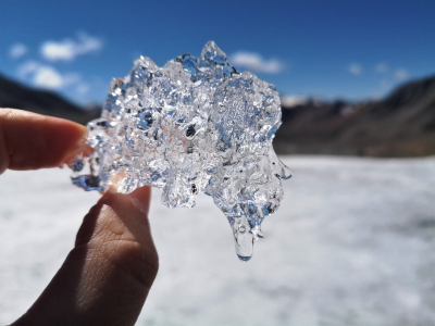 a piece of ice held into the sun by two fingers
