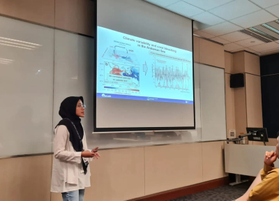 Hana standing in front of a screen in a conference room, giving an oral presentation