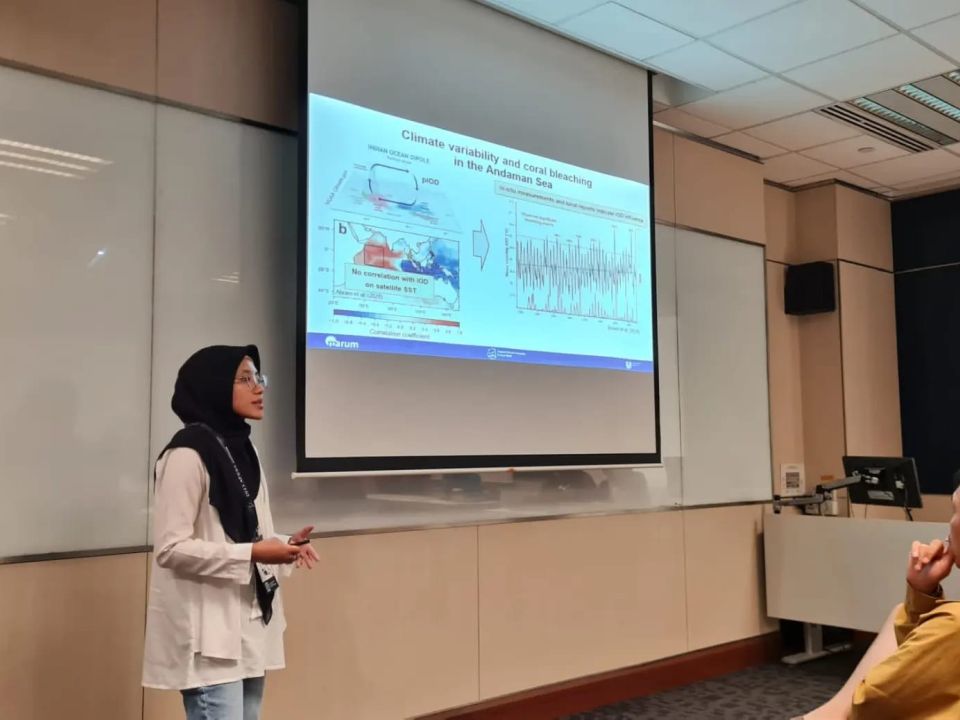 Hana in front of a screen in a conference room, giving an oral presentation