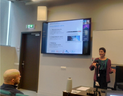 Lol standing next to a screen in a conference room givng a presentation