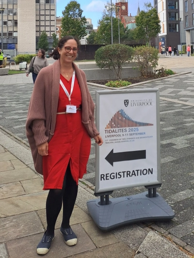 Alice in front of a poster showing the way to the conference registration