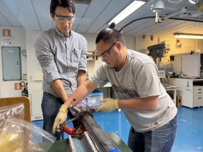 Matt Ikari (Physikalische Eigenschaften, rechts) und Hiroki Sone (Strukturgeologie) entnehmen Proben aus dem Bohrkern. Foto: JAMSTEC/IODP