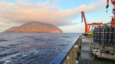 Abbildung zeigt Während der METEOR-Fahrt vor der griechischen Insel Milos: die Wasserschöpfer-Rosette und das AUV MARUM-SEAL an Deck, im Hintergrund die Vulkaninsel Antimilos. Foto: MARUM – Zentrum für Marine Umweltwissenschaften, Universität Bremen; S. I. Bühring